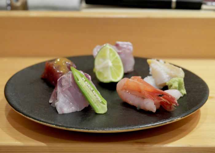 A plate of sushi and sashimi at Komatsu Yasuke, including prawn, tuna, wasabi, and a lime wedge..